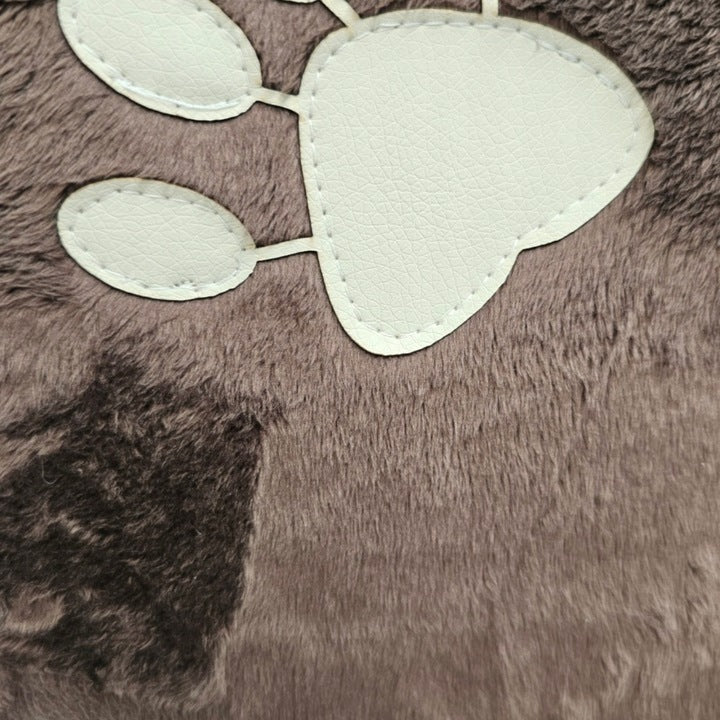 Small curly-haired dog sitting in a chocolate quilted dog car seat mounted to the front passenger chair with tan leather upholstery; plush interior and zippered sides with embroidered paw detail