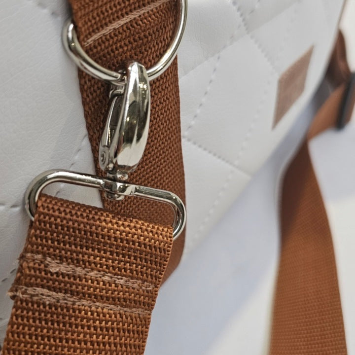 White quilted dog travel bag with brown shoulder straps and soft plush interior; — a stylish and secure pet carrier for small breeds.