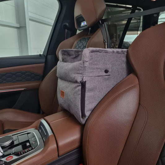 Grey dog car seat securely mounted between the front seats of a car with tan leather upholstery; features padded sides, side zip and a branded Golden Dog patch — designed for small pets to travel safely and stylishly